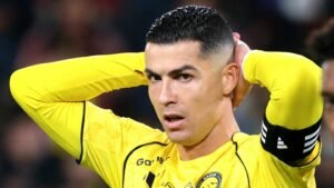 Cristiano Ronaldo in a yellow Al Nassr kit, holding his head with a focused expression during a match, highlighting his intense gameplay.