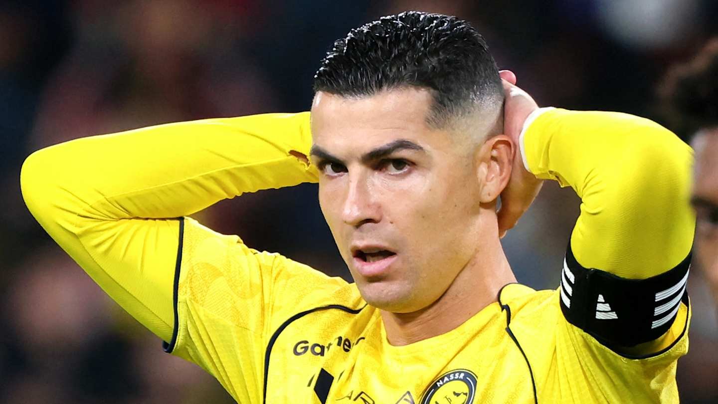 Cristiano Ronaldo in a yellow Al Nassr kit, holding his head with a focused expression during a match, highlighting his intense gameplay.