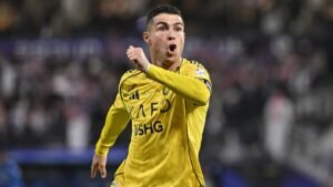 كريستيانو رونالدو يحتفل بحماس مرتديًا قميص النصر الأصفر اللامع خلال المباراة، محاطًا بحشد جماهيري ضبابي الخلفية.