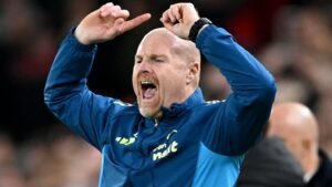 Sean Dyche uit gepassioneerd zijn frustratie aan de zijlijn tijdens een wedstrijd, gekleed in een blauw jasje met teambranding.