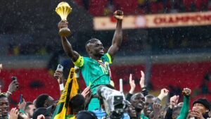 Sadio Mané viert het hijsen van de AFCON-trofee, omringd door teamgenoten in groene shirts, overgoten door regen en vreugde.