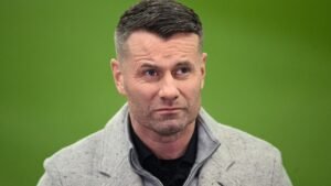 Shay Given lijkt nadenkend, gekleed in een grijze trui over een zwart shirt, tegen een groene achtergrond, terwijl hij zijn recente opmerkingen bespreekt.