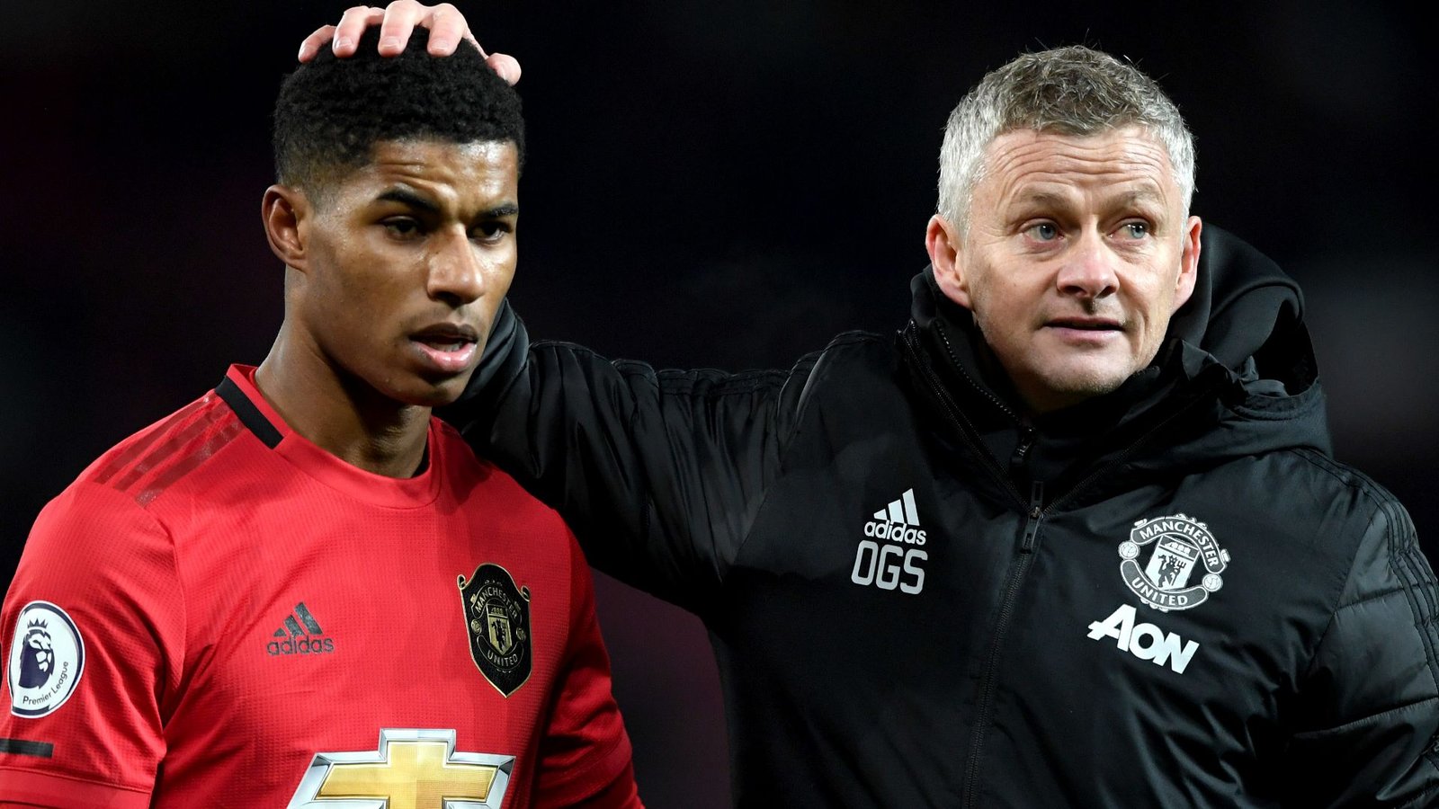 Marcus Rashford in Manchester United's rode outfit ziet er bezorgd uit terwijl Ole Gunnar Solskjær, gekleed in een zwarte jas, hem geruststelt.