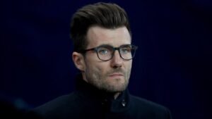 Rapha Wicky, portant un manteau noir et des lunettes, regarde pensivement devant lui, laissant entrevoir son futur rôle au Sporting KC.