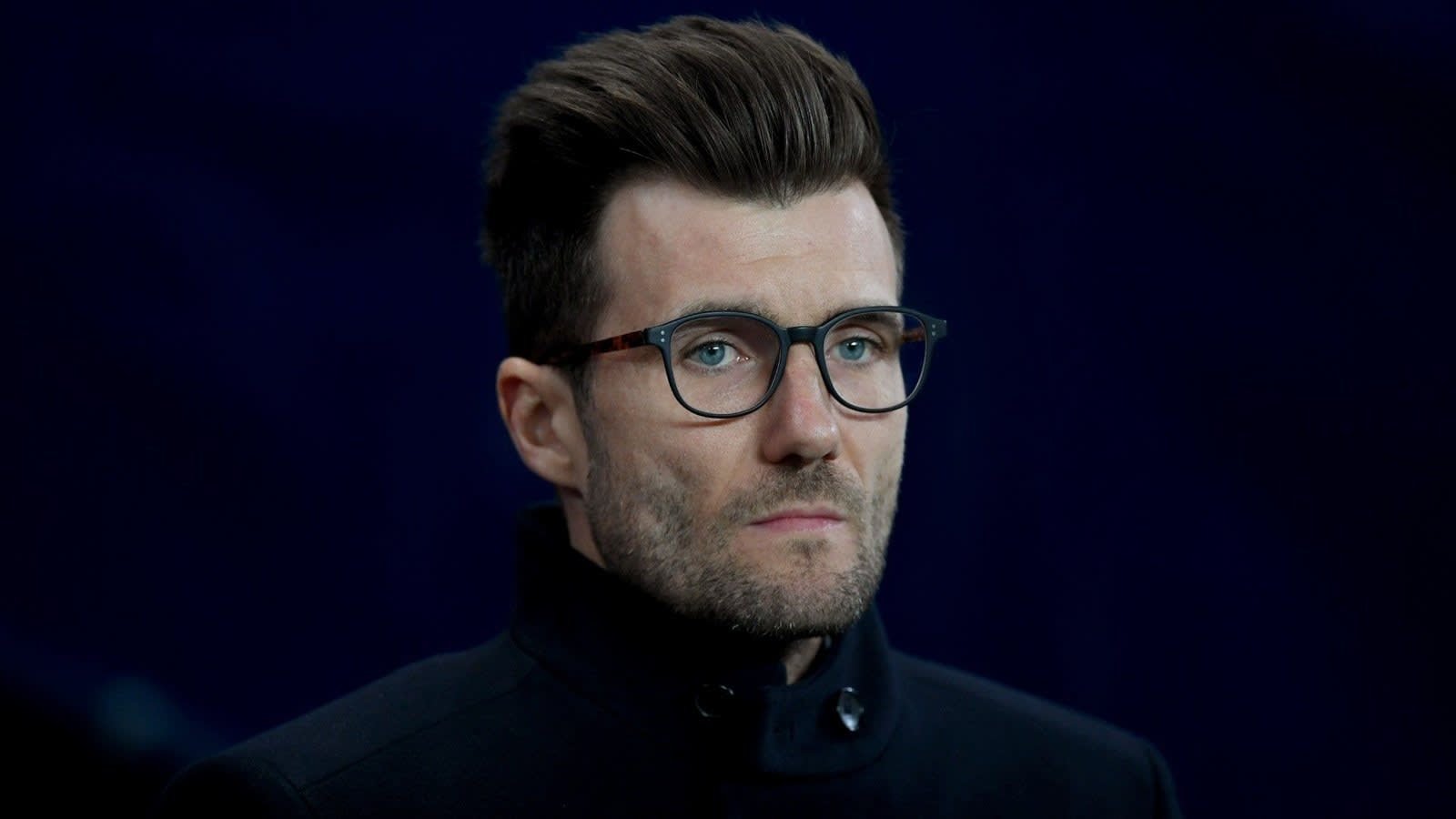 Rapha Wicky, portant un manteau noir et des lunettes, regarde pensivement devant lui, laissant entrevoir son futur rôle au Sporting KC.