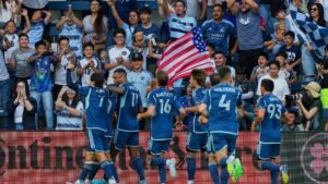 Spelers van Sporting Kansas City vieren een doelpunt, geflankeerd door opgewonden fans in teamtenues, zwaaiend met een Amerikaanse vlag en juichend in een uitverkocht stadion.