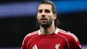 Un joueur de Liverpool aux cheveux longs porte le maillot rouge du club, l'expression concentrée, alors qu'il se prépare pour un match à venir.