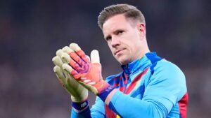 Marc-André ter Stegen, vêtu du maillot bleu et rouge éclatant du Barça, frappe dans ses mains avec des gants de gardien colorés, le regard concentré vers la foule.