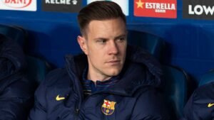 Marc-André ter Stegen in een Barcelona-jack, geconcentreerd en in gedachten verzonken op de bank, met het teamlogo zichtbaar op zijn kleding.
