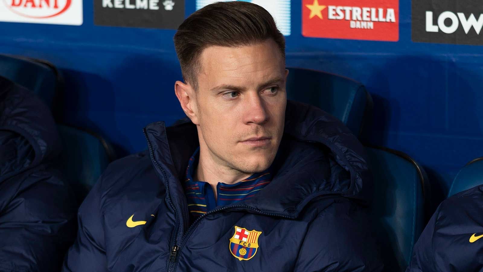 Marc-André ter Stegen in een Barcelona-jack, geconcentreerd en in gedachten verzonken op de bank, met het teamlogo zichtbaar op zijn kleding.