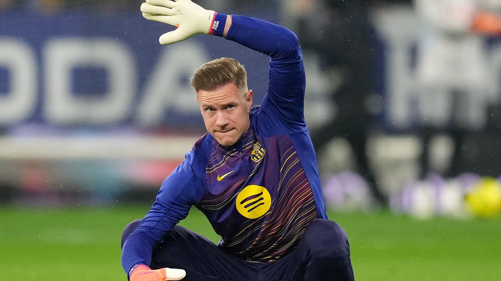 Marc-André ter Stegen in een blauw Barcelona-tenue, zich voorbereidend op het spel met één opgeheven hand, toont zijn geconcentreerde uitdrukking en keepershandschoenen.