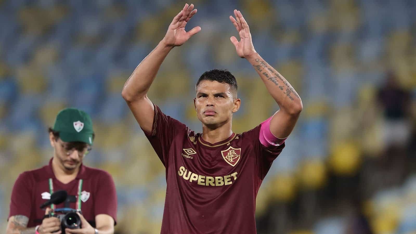 Thiago Silva zwaait na de wedstrijd naar de fans, gekleed in het kastanjebruine tenue van Fluminense met de aanvoerdersband, in een levendige stadionsetting.