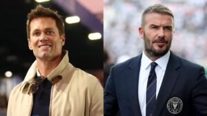 Tom Brady, souriant dans une veste beige, se tient aux côtés de David Beckham, vêtu d'un costume sombre arborant le badge d'Inter Miami, les deux hommes engagés dans une conversation.