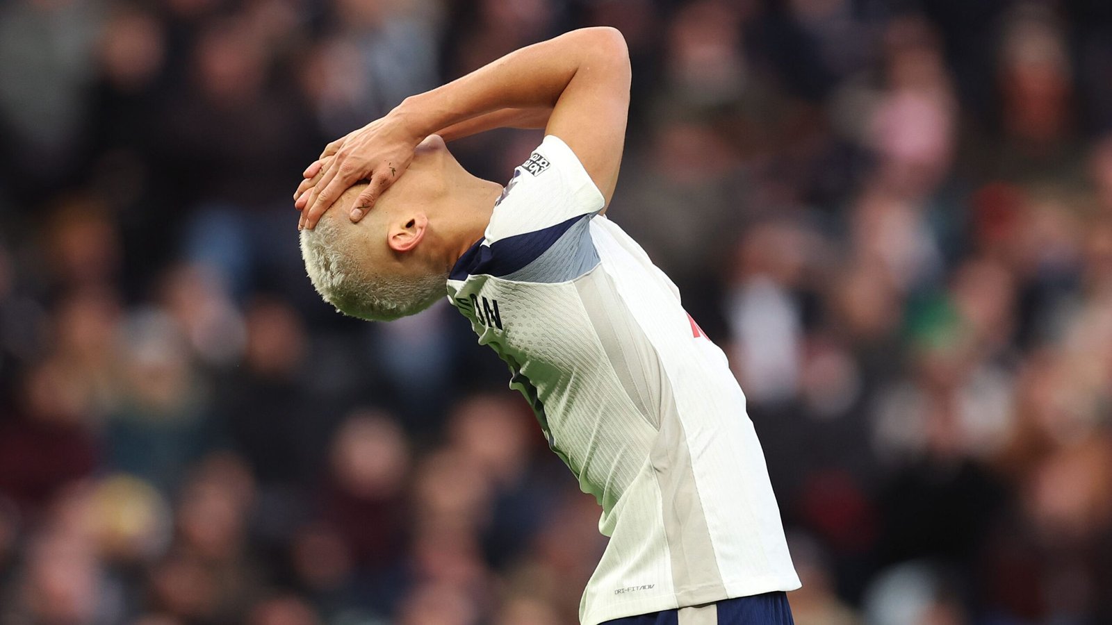 Richarlison van Tottenham Hotspur toont frustratie na een opgelopen blessure tijdens een wedstrijd, met wazige fans op de achtergrond.