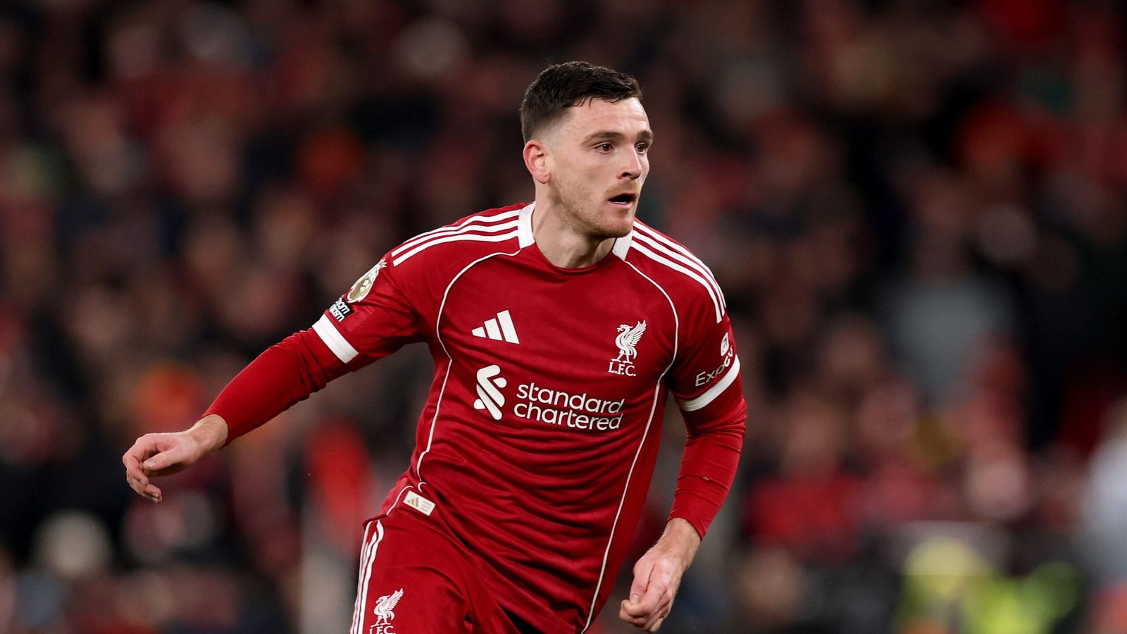 Liverpool's Andy Robertson in een levendig rood tenue, sprintend over het veld tijdens een wedstrijd, met vastberadenheid en focus.