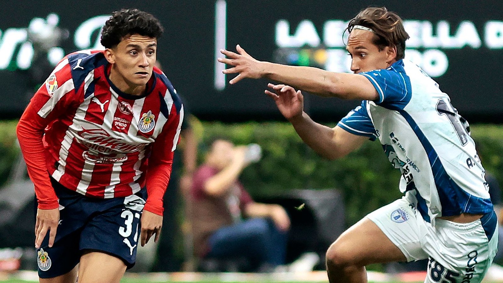 Un joueur de Chivas, en rayures rouges et blanches, évite un défenseur en bleu et blanc lors d'un moment tendu d'un match de championnat mexicain.