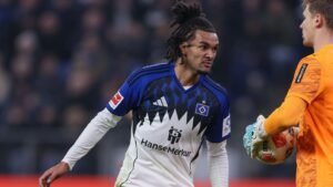 Un joueur du Hannover 96, vêtu du maillot domicile bleu et noir, réagit lors d'un match de Bundesliga en interagissant avec un gardien de but portant une tenue orange.