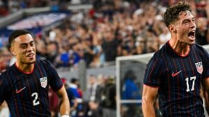 Des joueurs américains célébrant un but, portant leurs maillots rayés bleu marine et rouge, avec une foule enthousiaste en arrière-plan, illustrant l'esprit d'équipe.