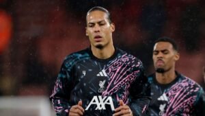 Virgil van Dijk in een opvallend Liverpool-trainingspak, geconcentreerd tijdens een regenachtige warming-up, met een teamgenoot op de achtergrond.