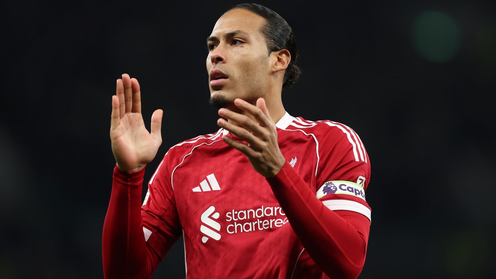 Virgil van Dijk in een rood Liverpool-tenue gebaart met zijn handen en toont vastberadenheid en leiderschap tijdens een wedstrijd.