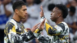 Vinícius Jr. et Jude Bellingham partagent un moment d'encouragement, portant tous deux des maillots à motifs frappants, dans l'atmosphère vibrante d'un stade.