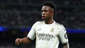 Vinícius Júnior, portant le maillot blanc du Real Madrid avec le logo "Emirates Fly Better", concentré sur le terrain pendant un match, affichant de la détermination.