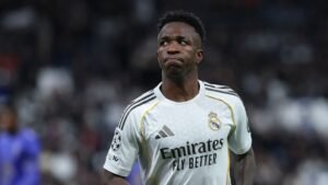 Vinícius Júnior van Real Madrid, gekleed in het witte clubtenue, kijkt bedachtzaam tijdens een wedstrijd, reflecterend op de gebeurtenissen in het spel.