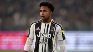 Weston McKennie wearing Juventus' black and white striped kit, focused on the match in a stadium with blurred crowd background.