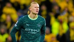 Erling Haaland in zijn groene Manchester City-tenue, geconcentreerd kijkend te midden van een menigte geelgeklede fans tijdens een wedstrijd.