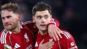 Liverpool players celebrate a goal together, wearing their iconic red kits with white accents, showcasing team camaraderie on the pitch.