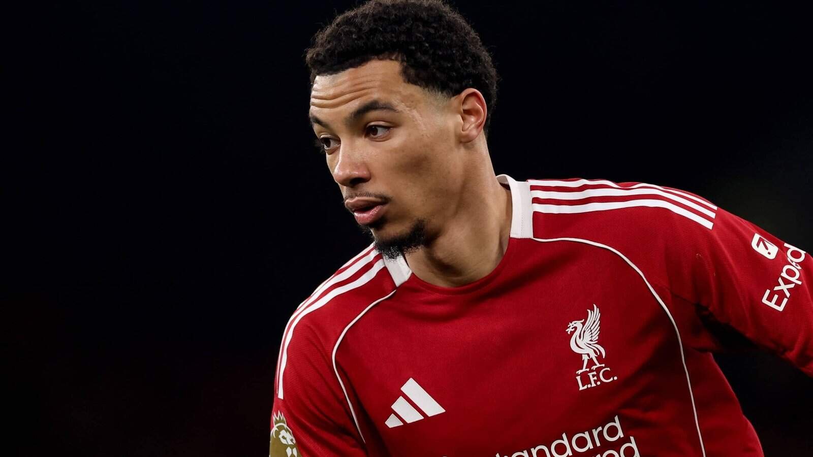 Trent Alexander-Arnold dans le maillot rouge de Liverpool, montrant de la détermination pendant un match, avec les lumières du stade illuminant la scène.