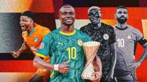 Sadio Mané in het groen tenue van Senegal houdt de AK-trofee vast, geflankeerd door spelers in oranje, zwart en grijze tenues die hun teams toejuichen.