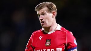 Le capitaine de Wrexham, James McClean, vêtu d'une tenue rouge, observe attentivement pendant un match, illustrant l'esprit d'équipe et la détermination.
