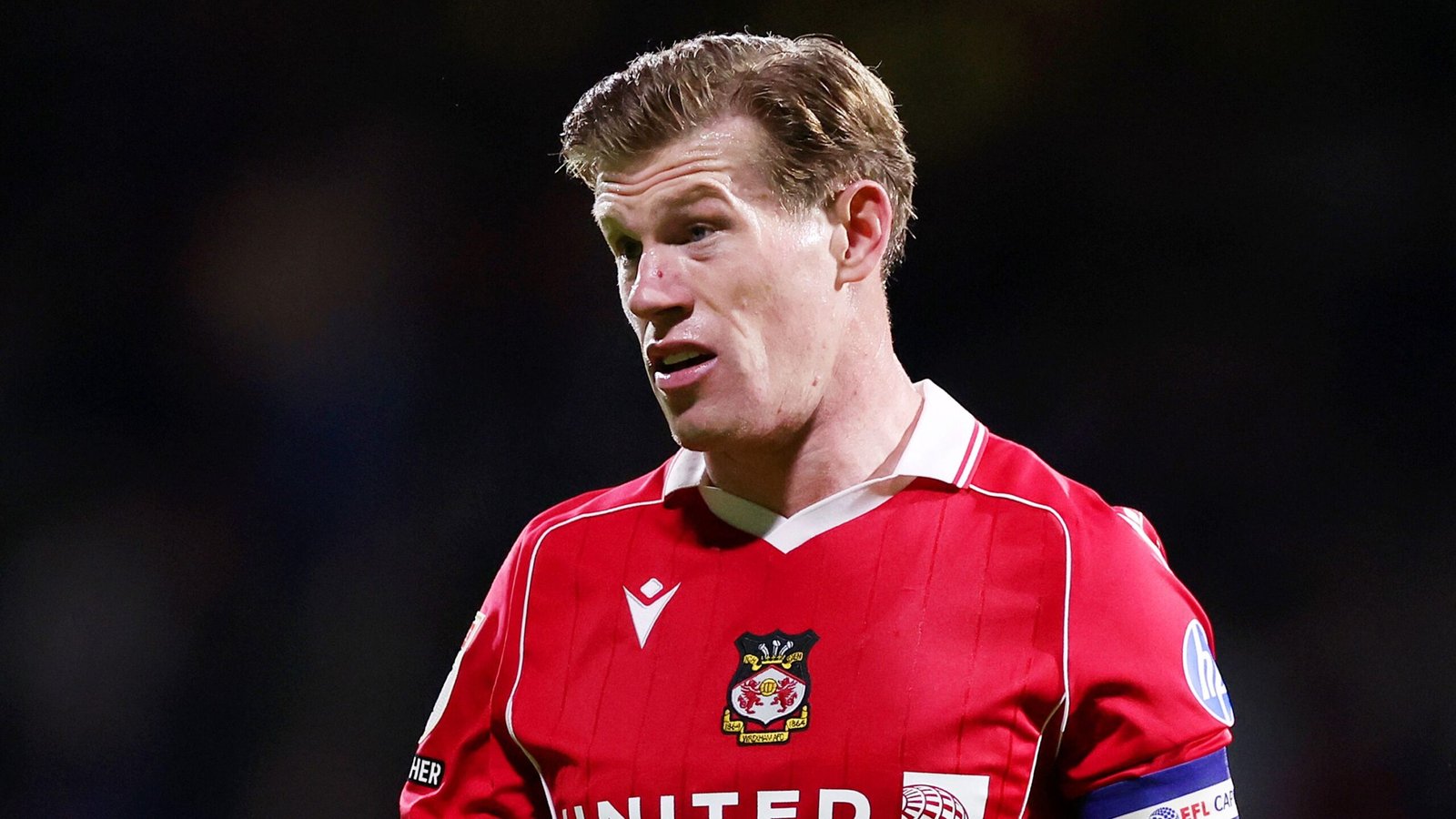 Le capitaine de Wrexham, James McClean, vêtu d'une tenue rouge, observe attentivement pendant un match, illustrant l'esprit d'équipe et la détermination.
