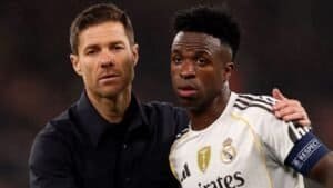 Xabi Alonso comforts Vinícius Júnior during a tense moment, both in Real Madrid kits, with a focused expression on the pitch.