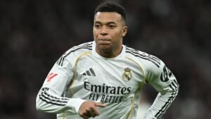 كيليان مبابي يرتدي قميص ريال مدريد الأبيض، مركزاً على أرض الملعب خلال مباراة، مع إبراز شعار النادي والراعي.