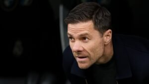 Xabi Alonso observeert aandachtig vanaf de zijlijn, gekleed in een donkere jas, met een geconcentreerde uitdrukking tijdens een wedstrijd.