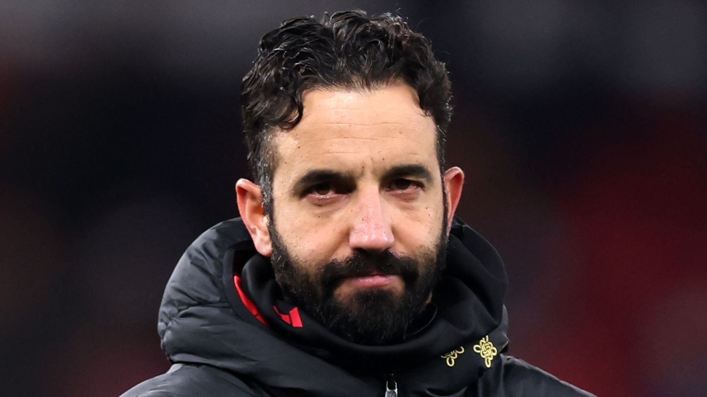 Un homme portant un manteau noir à capuche, arborant une barbe et des cheveux bouclés, le regard solennel, probablement dans un contexte footballistique.