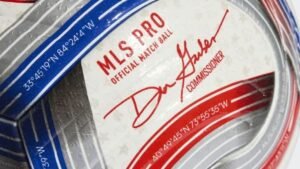 كرة المباراة الرسمية للدوري الأمريكي بتصميم رمادي مع خطوط حمراء وزرقاء، موقعة من المفوض دون جاربر، تعرض ميزاتها الفريدة.