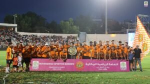 Spelers van Renaissance Sportive de Berkane vieren hun Botola Pro-kampioenschapsoverwinning 2024-2025, terwijl ze de trofee en een vlag vasthouden.