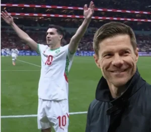 Moroccan player celebrating in a white kit with green and red details, while a smiling coach observes from the side during a match.