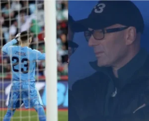 Zidane, portant le numéro 23 de gardien dans un kit bleu ciel, réagit avec frustration tandis qu'un entraîneur observe depuis le banc.