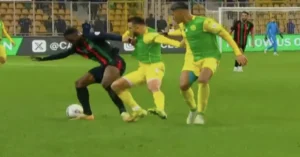 Moroccan player in black and red kit tussles with two players in green and yellow during an intense league match.