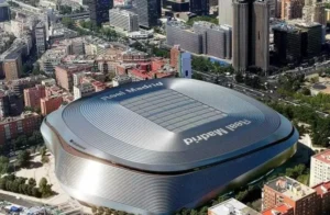 Aerial view of the Santiago Bernabéu Stadium, featuring its distinctive curved architecture and 'Real Madrid' signage, amidst a cityscape.