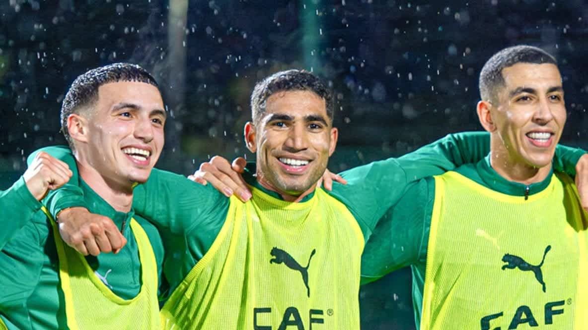 Moroccan football players celebrate joyfully in rain, wearing green training kits and commemorative bibs, embodying team spirit.