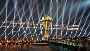 African Cup of Nations trophy illuminated by spotlights, surrounded by performers in traditional attire, showcasing the event’s festive atmosphere.