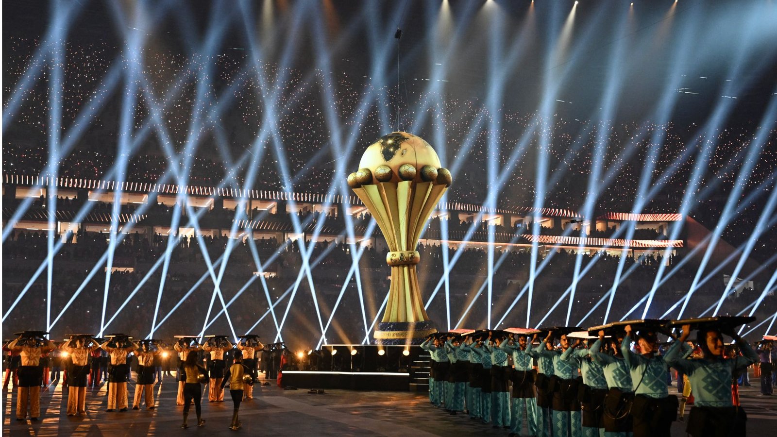 African Cup of Nations trophy illuminated by spotlights, surrounded by performers in traditional attire, showcasing the event’s festive atmosphere.