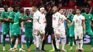 Spelers van Marokko en Senegal raken verwikkeld in een verhitte scène tijdens de wedstrijd, met een scheidsrechter die tussenbeide komt, tegen een levendig stadiondecor.