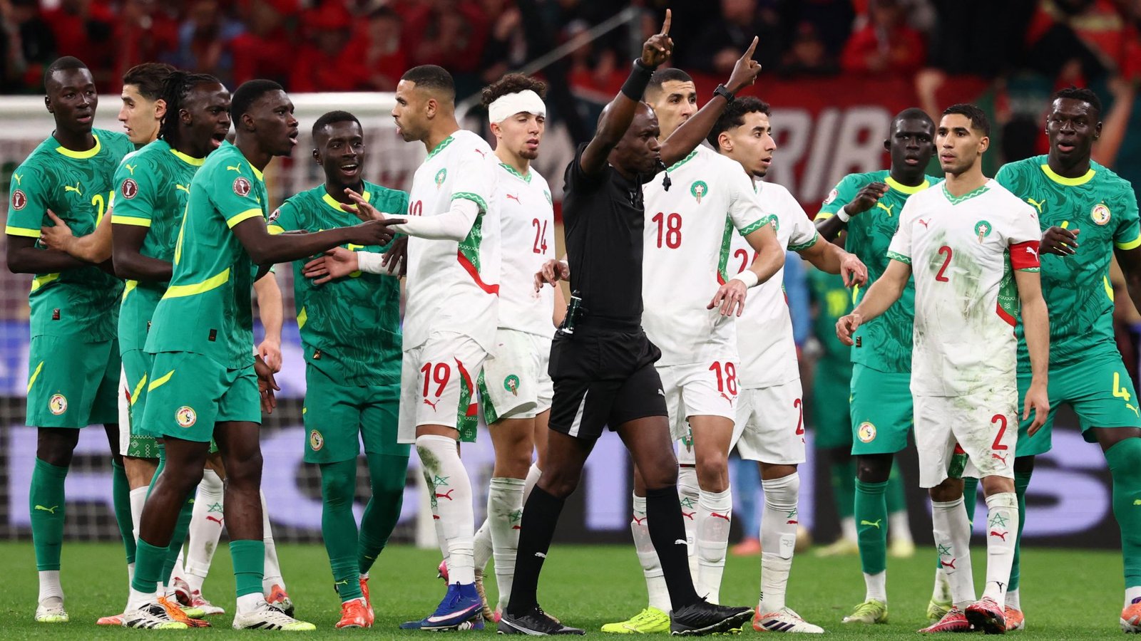 Spelers van Marokko en Senegal raken verwikkeld in een verhitte scène tijdens de wedstrijd, met een scheidsrechter die tussenbeide komt, tegen een levendig stadiondecor.