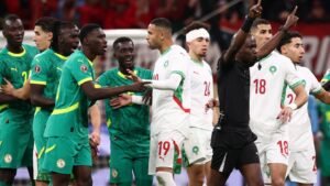 Les joueurs marocains et sénégalais s'engagent dans un moment tendu pendant un match, arborant les tenues de l'équipe nationale et des expressions intenses.